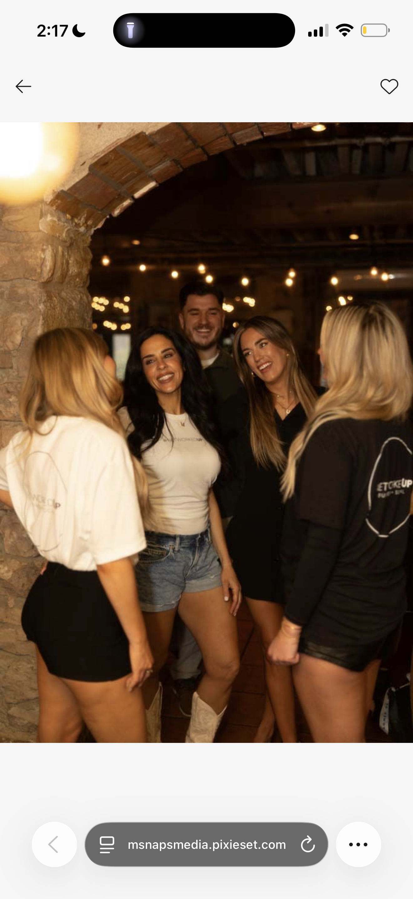 A group of five people gathered inside a warmly lit rustic venue, smiling and talking, with string lights hanging overhead.