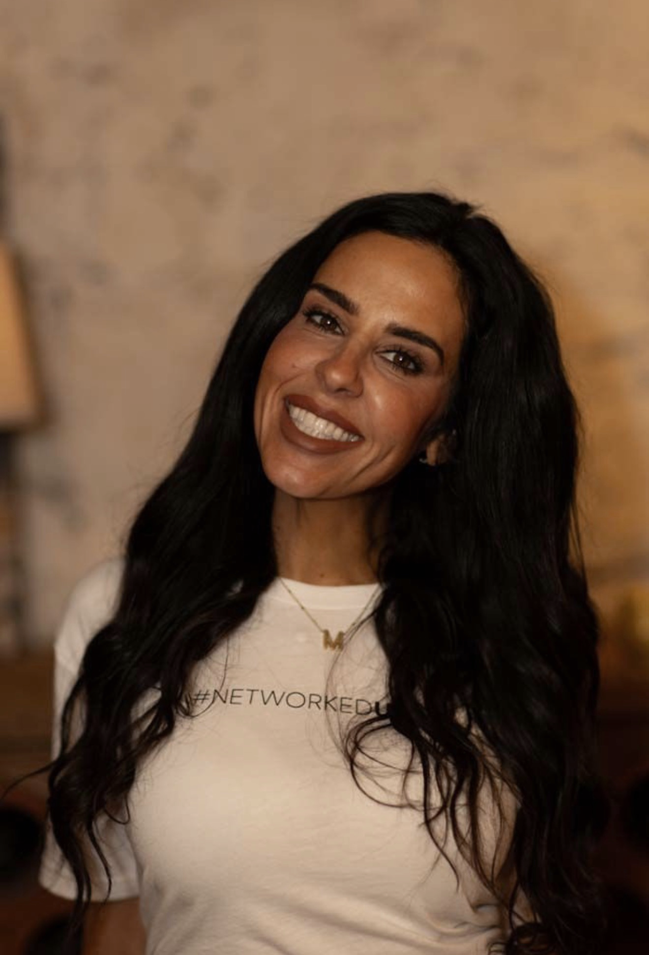 Woman with long dark wavy hair smiling and wearing a white T-shirt with hashtag #NETWORKEDU.