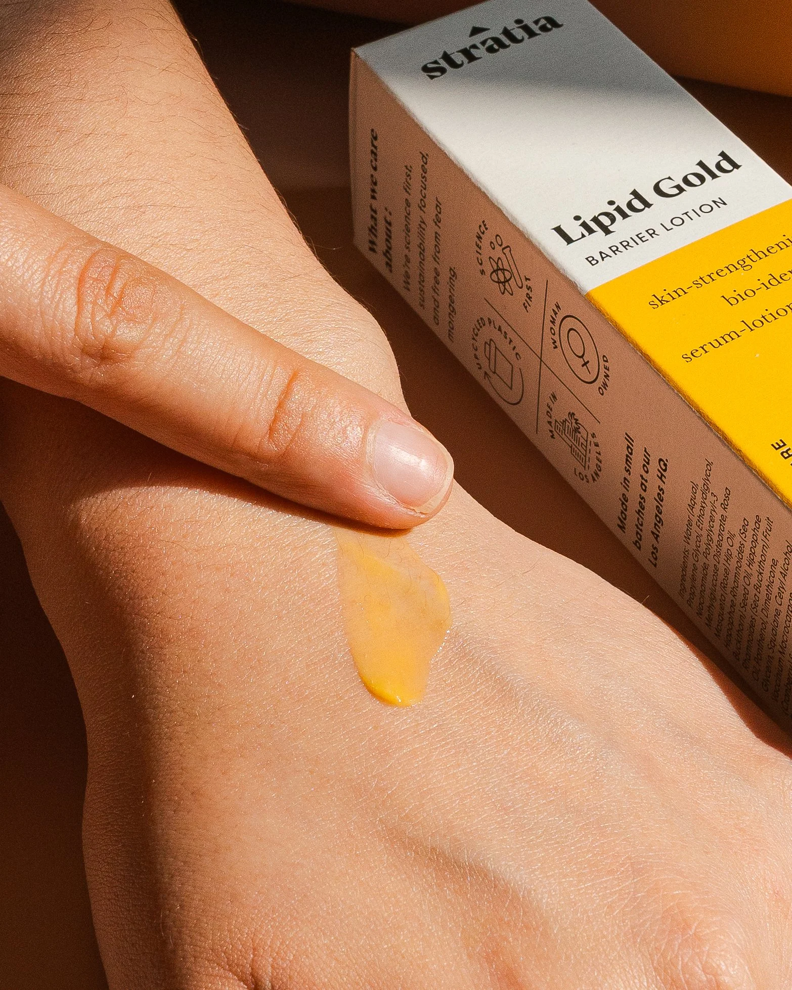 A person applying Lipid Gold barrier lotion on their arm. The lotion is yellow and has a creamy texture.