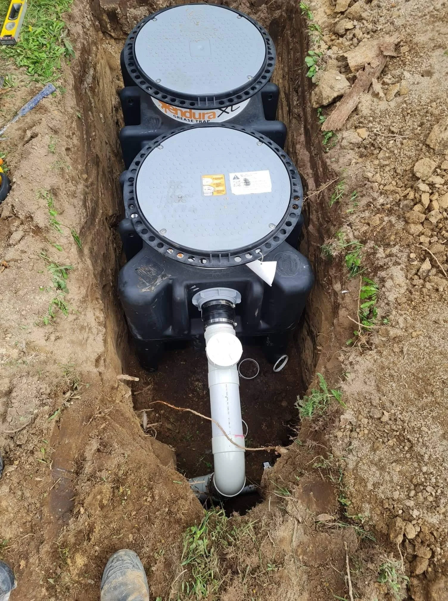 Underground grease trap and sewage pipe installation in a trench in dirt and soil.