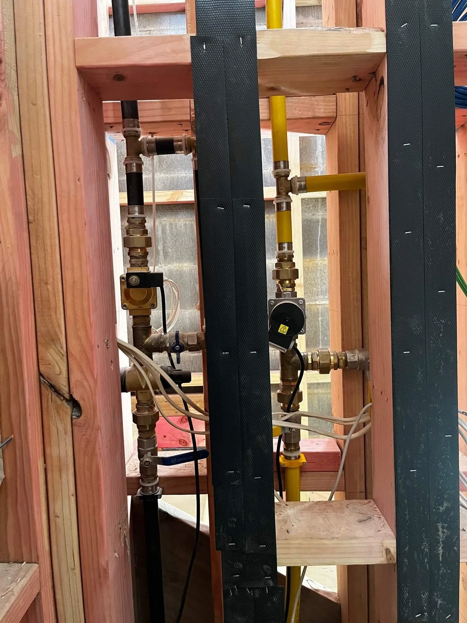 View inside a building wall framed with wood, showing plumbing pipes and fittings for water supply or heating system.