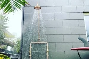 Shower head mounted on exterior wall with water flowing down.