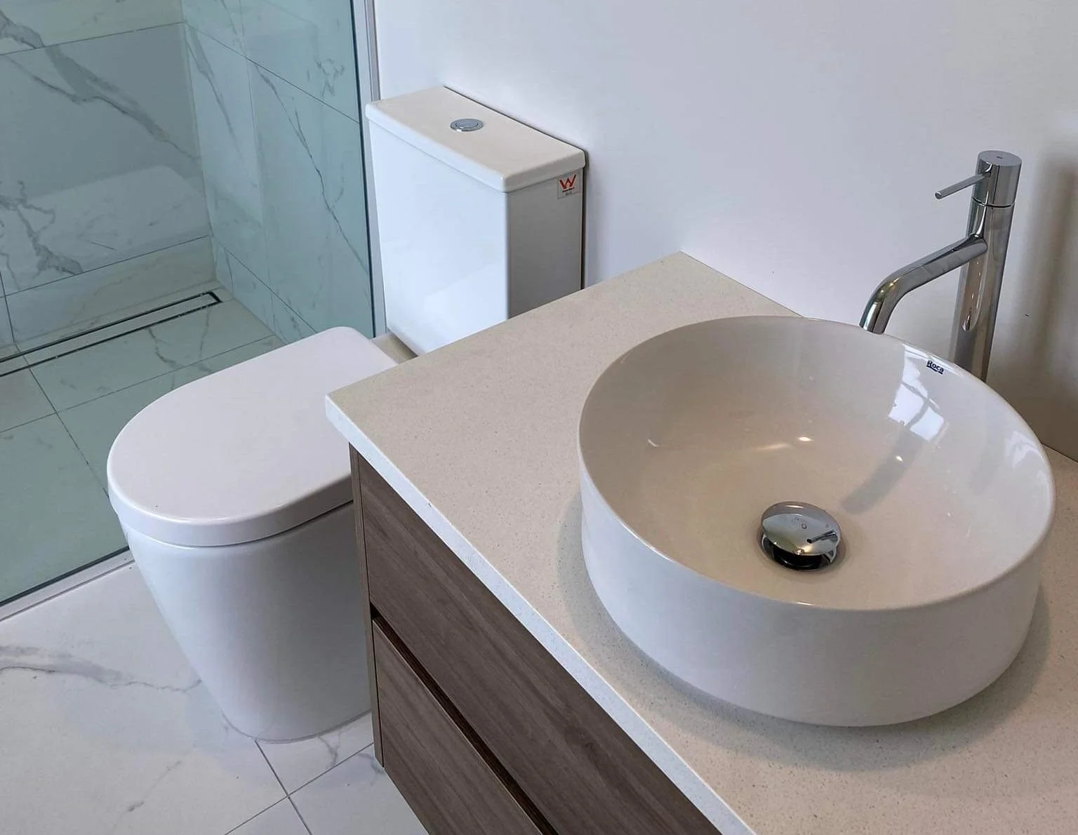 Modern bathroom with vessel sink on countertop, brown wooden cabinet, white toilet, and walk-in shower with glass enclosure.