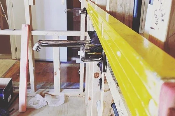 A partially constructed room with exposed wooden framing, a yellow measuring tape, and a kitchen sink with a faucet installed.