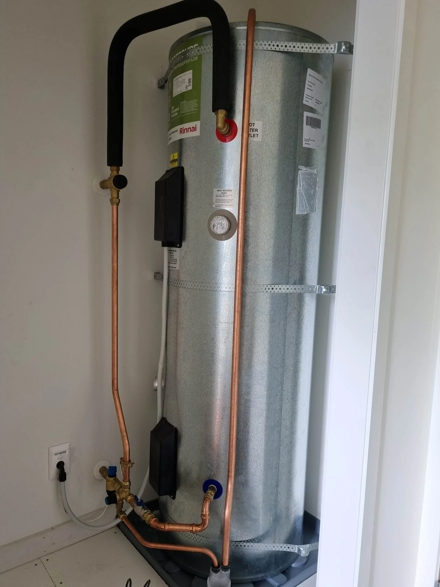 A water heater with copper pipes and plumbing connections inside a utility closet.