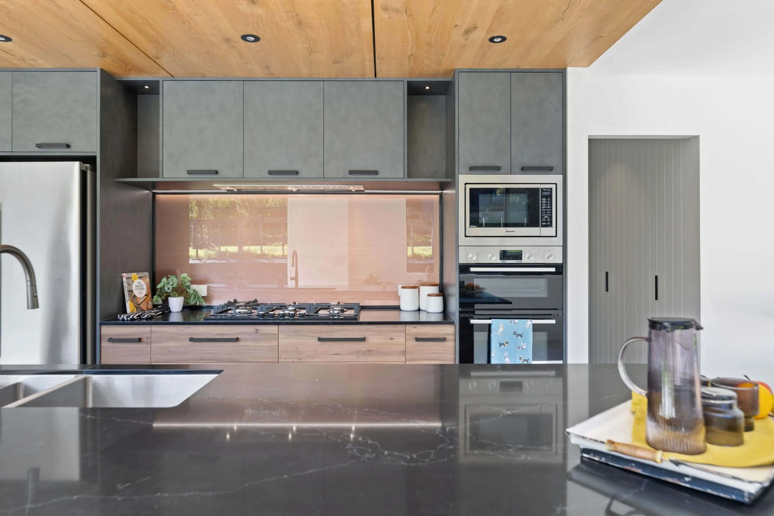 A modern kitchen with gray cabinets, wooden ceiling, and stainless steel appliances, including a microwave and an oven, with a countertop in the foreground.