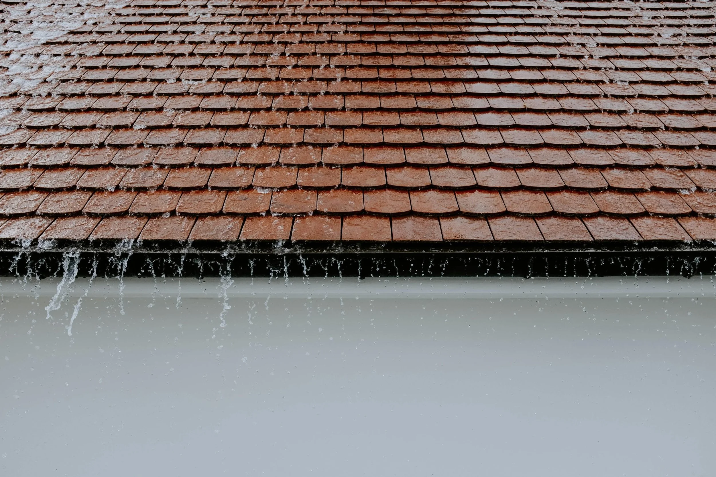 Rainwater dripping from a brown shingle roof.