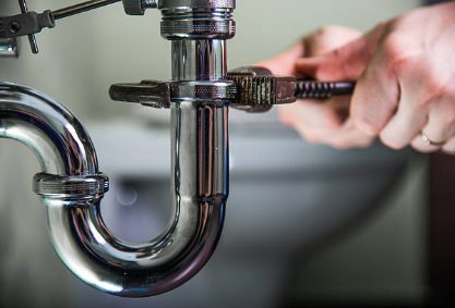 A person tightening a pipe under a sink with a wrench.