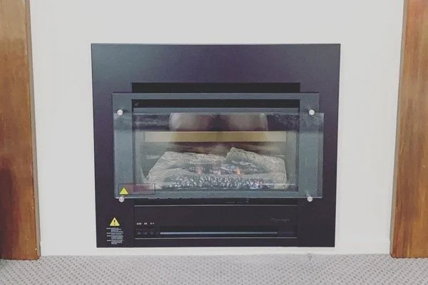 Electric fireplace with glass front, built into wall, with simulated flames and logs inside.