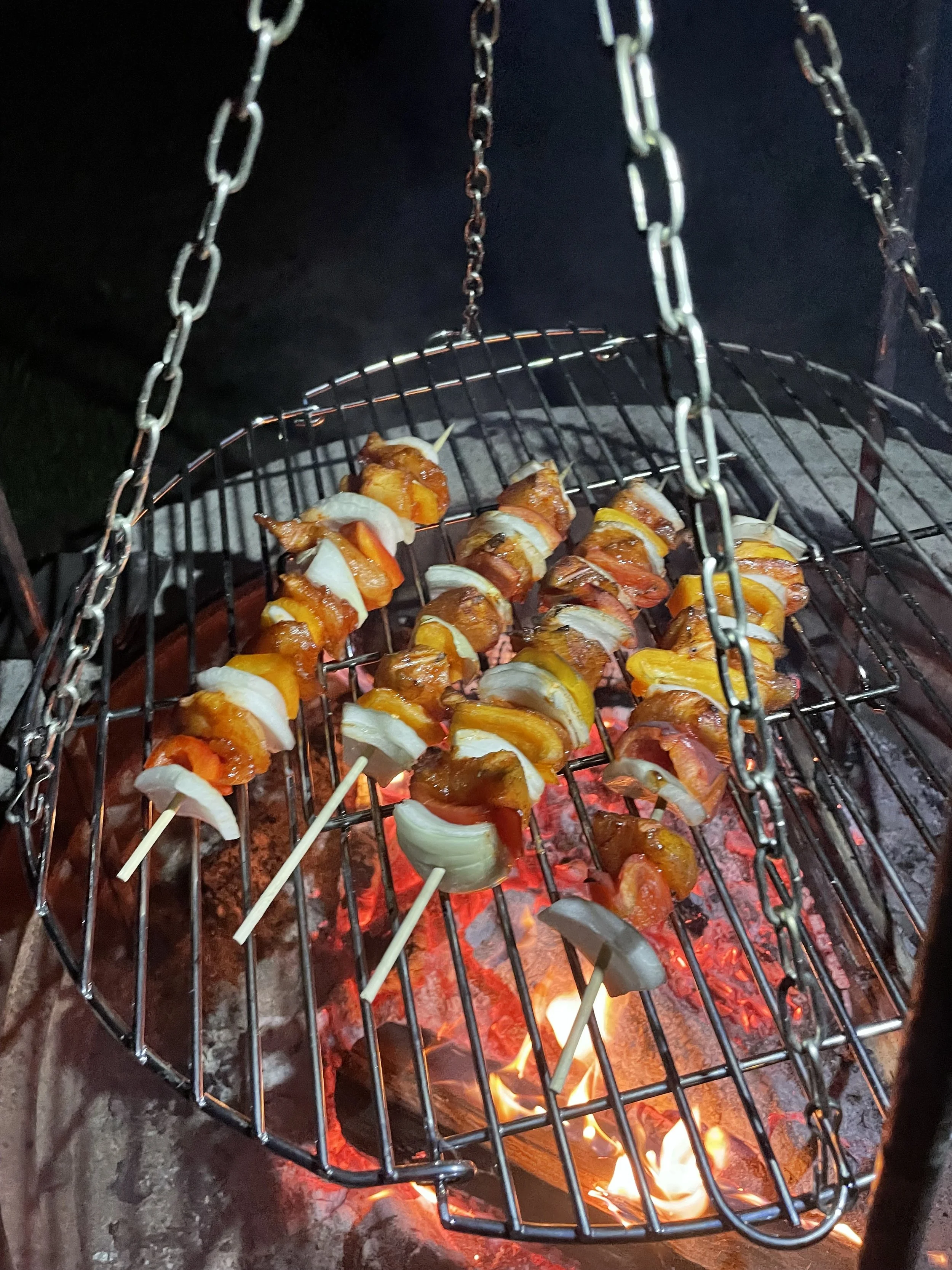 Skewers of bacon-wrapped vegetables cooking on a grill over red-hot coals.