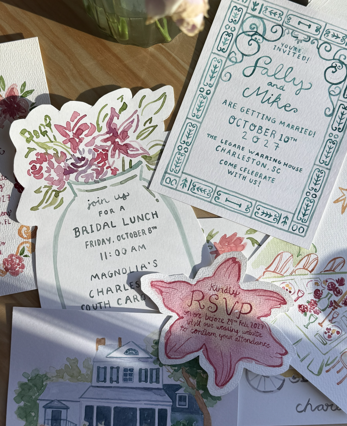 A collection of watercolor wedding and event invitations and RSVP cards, featuring floral designs and decorative borders, displayed on a wooden surface.