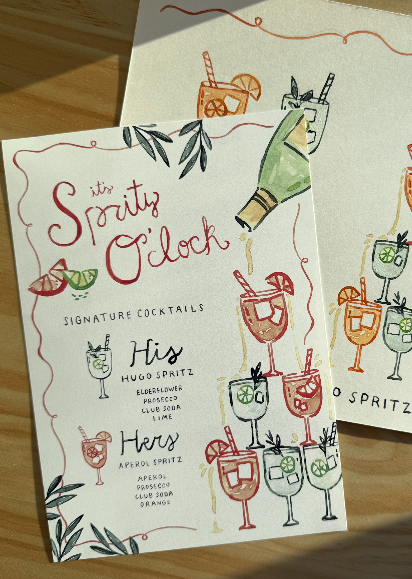 A colorful menu titled 'It's Spritz O'clock' featuring illustrations of spritz cocktails with lime, orange, and lemon garnishes. The menu lists signature cocktails: Hugo Spritz with elderflower, prosecco, club soda, lime, and Her Spritz with aperol, 