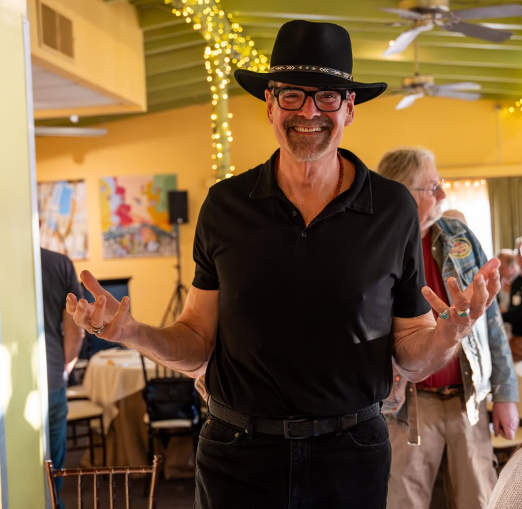 A smiling man in a black shirt and black cowboy hat.