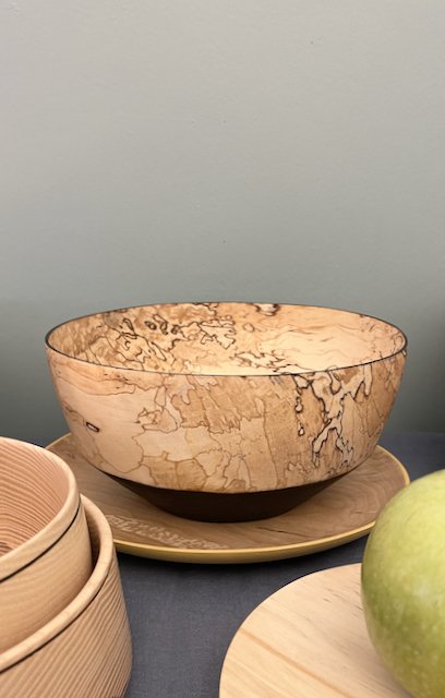 A large beige and brown marbled ceramic bowl on a yellow plate, with a green apple and stacked wooden bowls nearby.