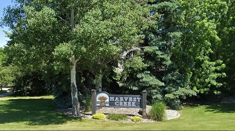 A sign reading 'Harvest Creek' surrounded by grass, trees, and landscaping.