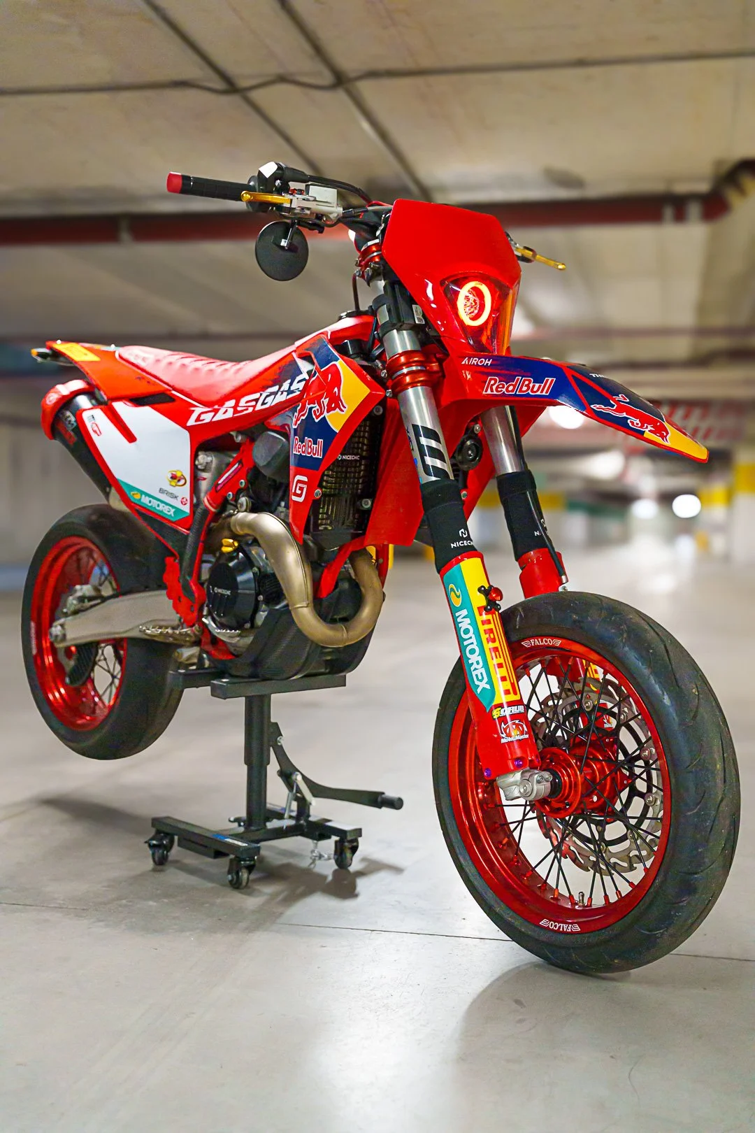 Moto da Cross Red Bull con sponsor Pirelli, in un parcheggio, sostenuta da un supporto.