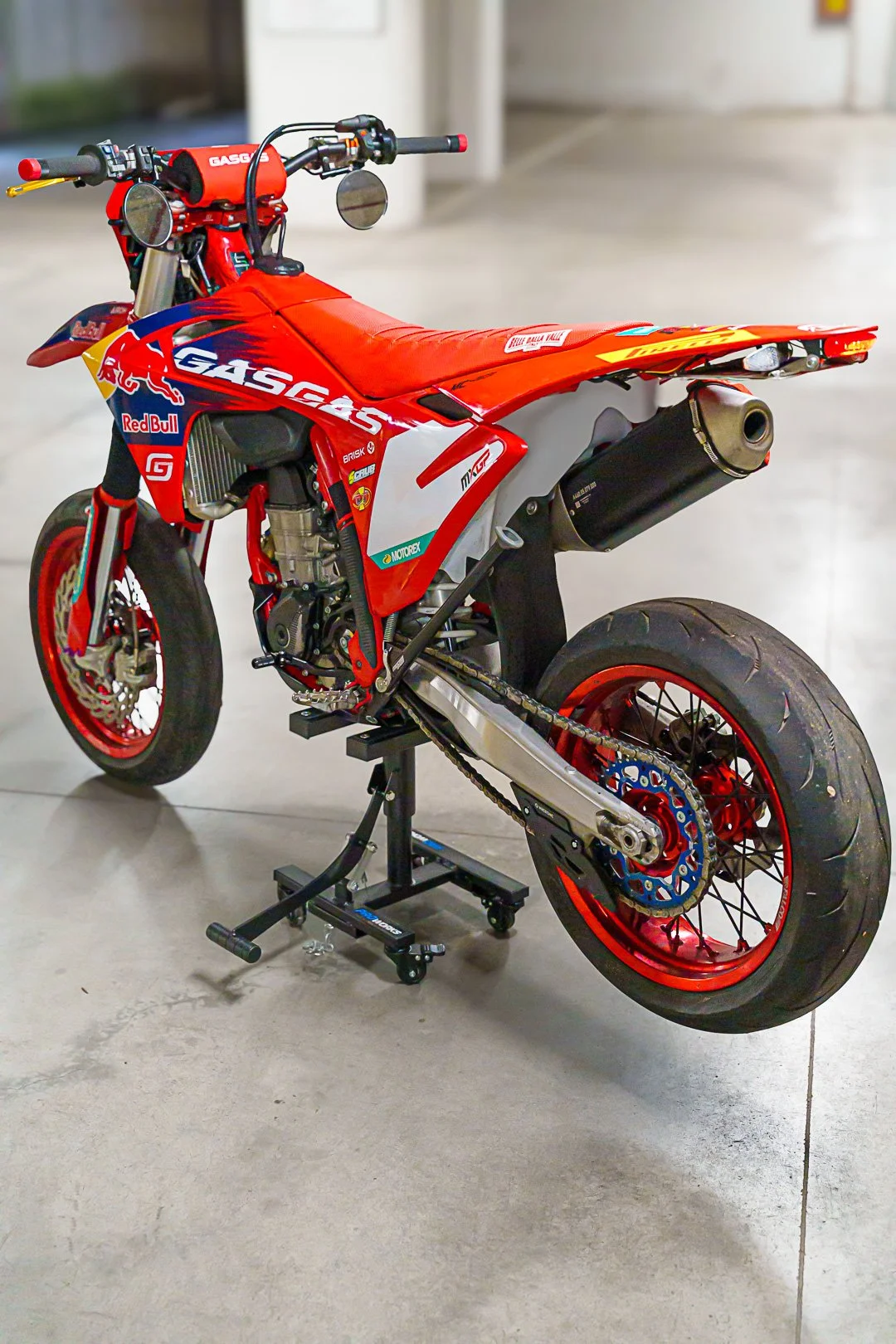 Motocicletta da corsa rossa con sponsor Red Bull e GasGas, vista di profilo in un ambiente interno.