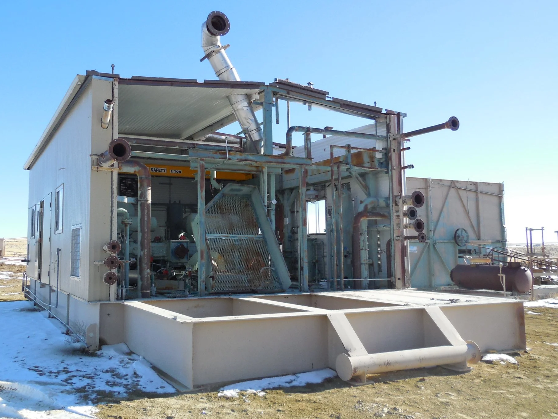 Industrial equipment with pipes and a safety label on a snowy ground in an open outdoor setting.