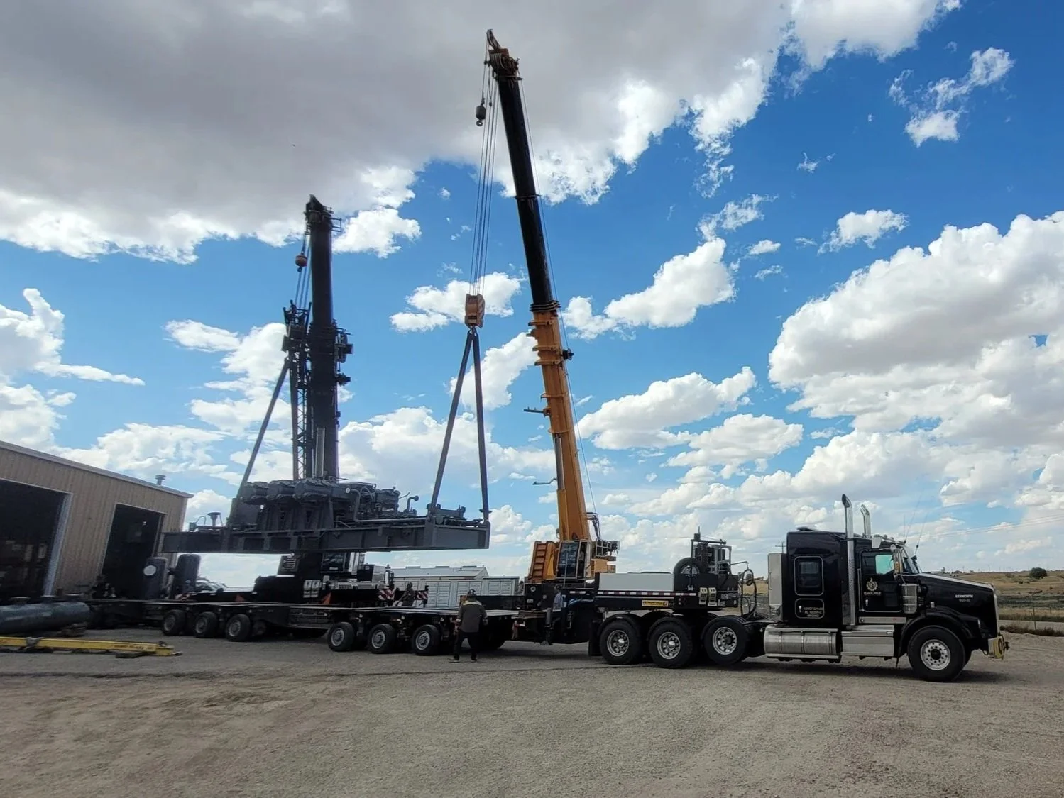 Large crane truck lifting a tall industrial structure outdoors under a partly cloudy sky.