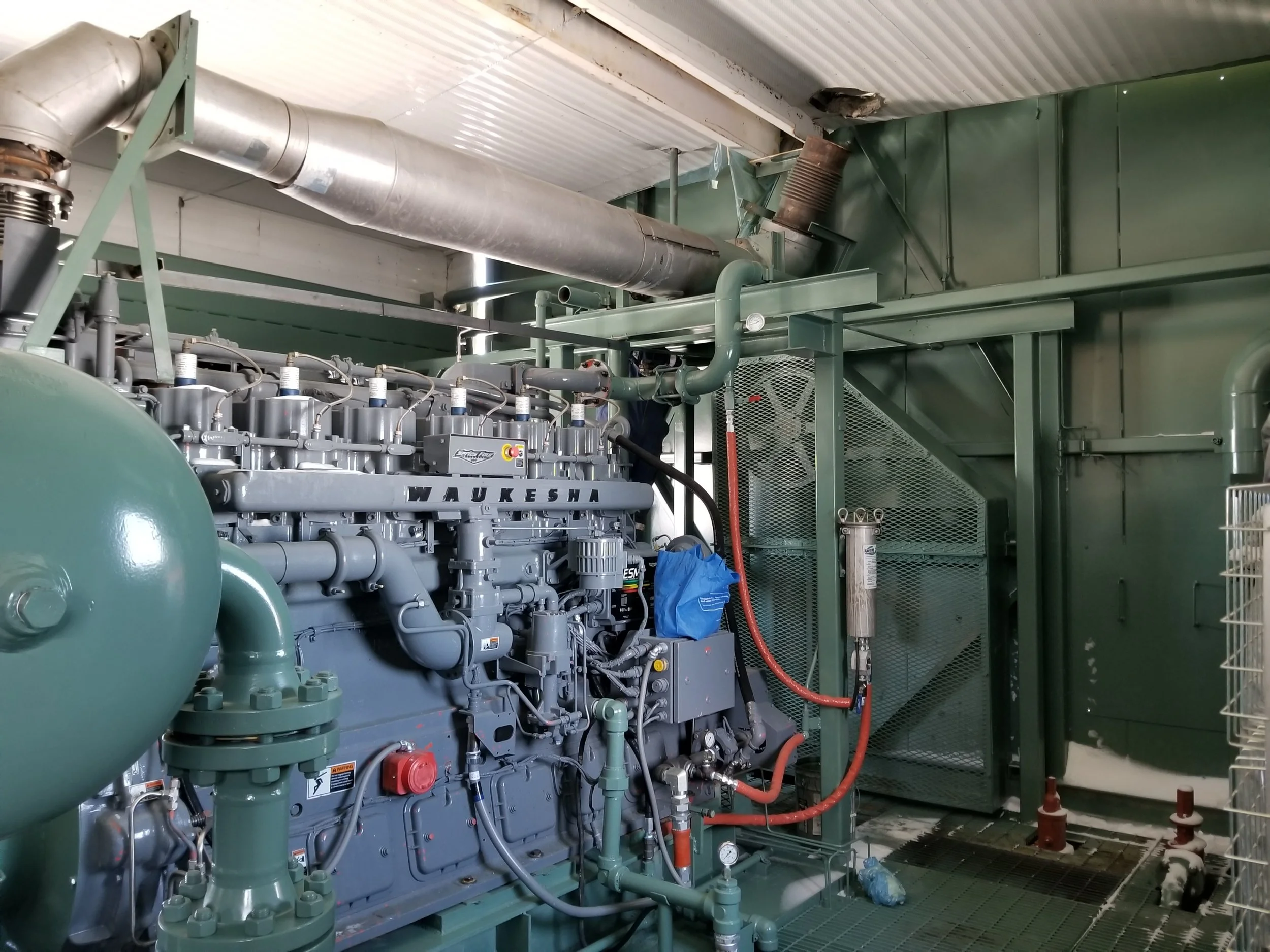 Industrial engine or mechanical equipment inside a facility with pipes and ventilation ducting.
