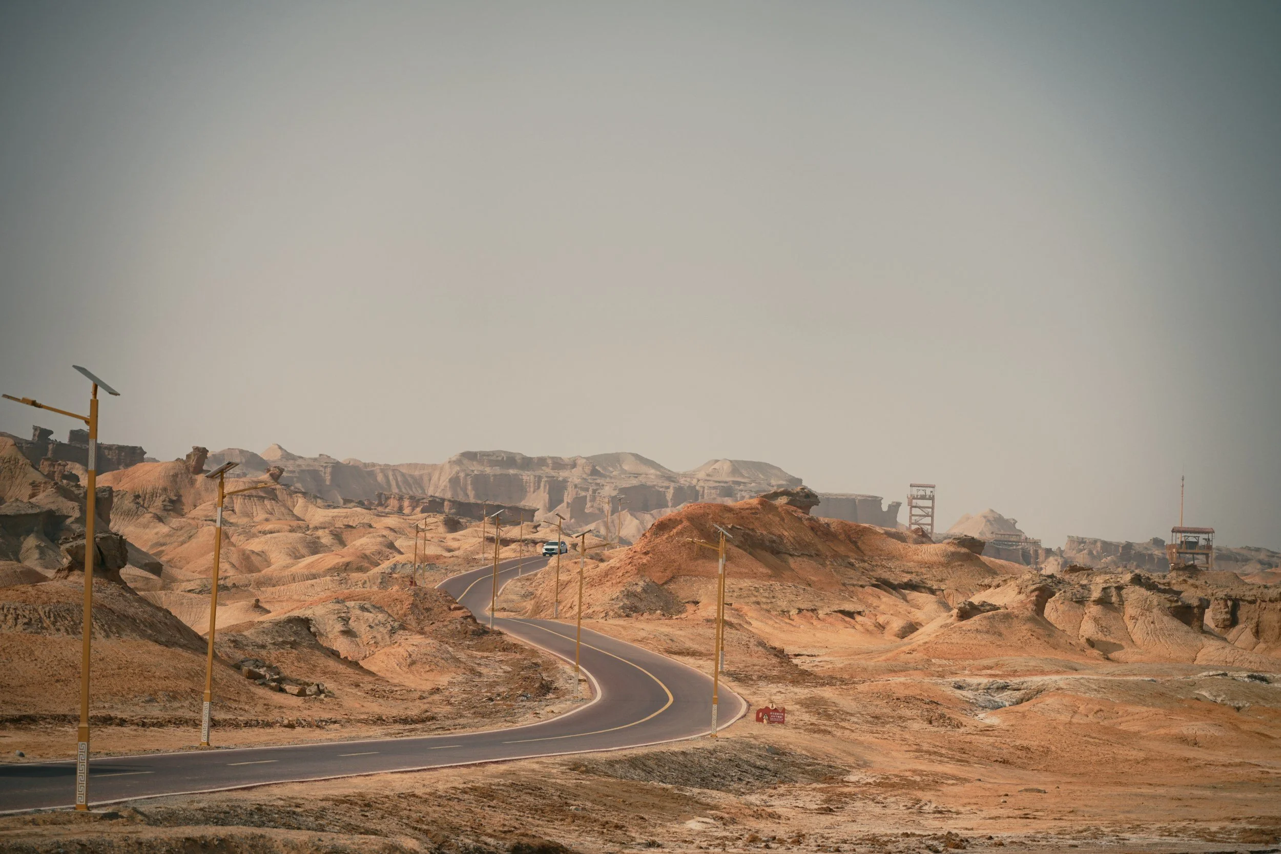 Winding road through desert landscape with scattered hills, sand, and rock formations, and solar-powered streetlights along the road.
