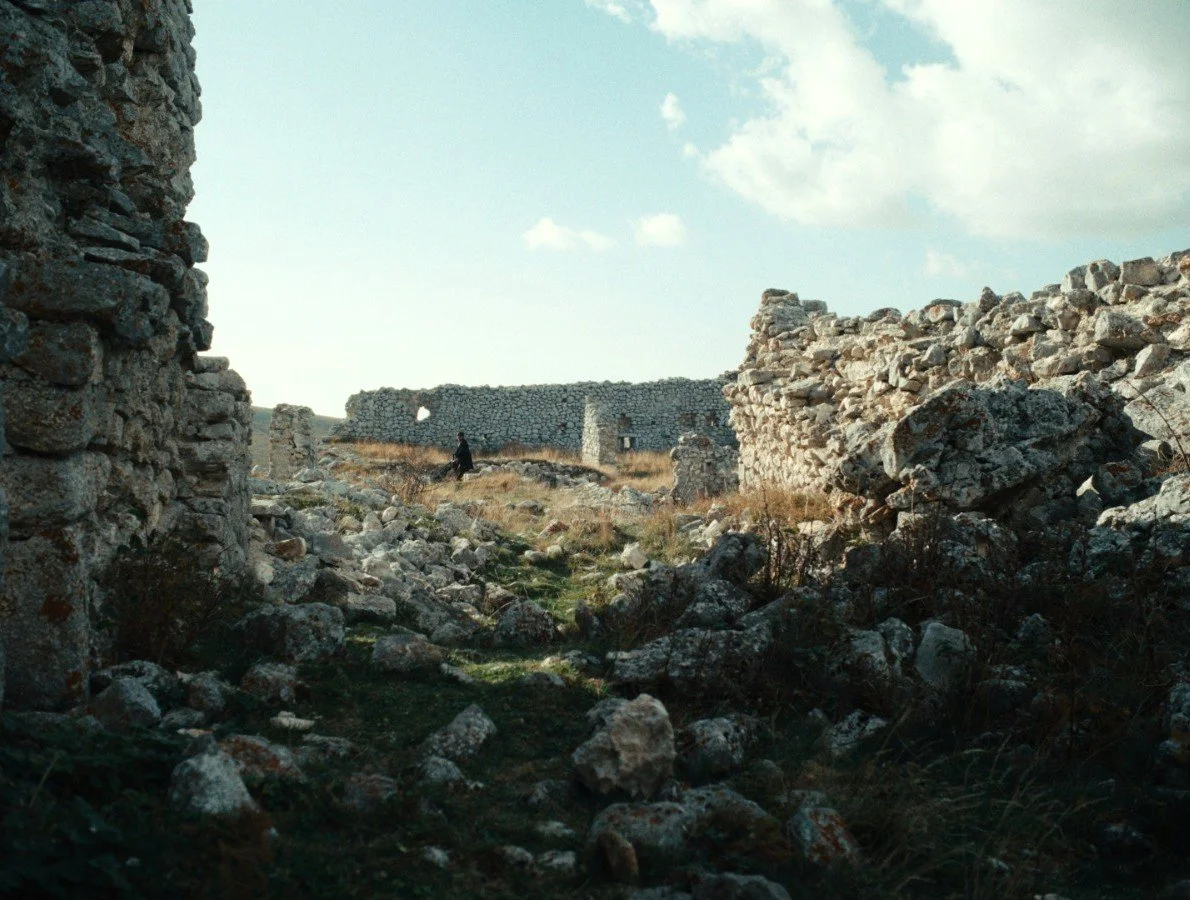 Rovine di un'antica struttura in pietra con un cielo nuvoloso sopra, e una persona in lontananza tra i resti.