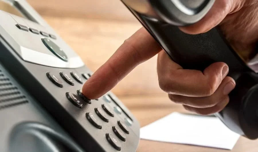 A person pressing a button on a landline telephone.