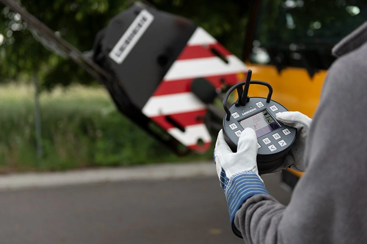 A technician is holding a remote control device in front of a utility or traffic sign with a blurred background of greenery and a road.