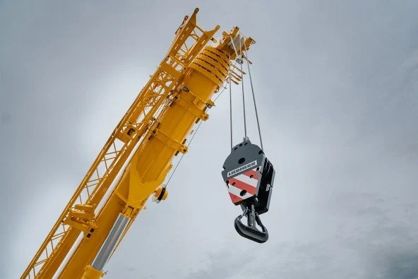 A large yellow crane lifting a hook and a suspended load against a cloudy sky.