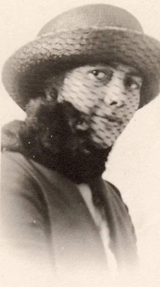 Close up black-and-white portrait of a young woman in early twentieth-century attire in a veiled hat.