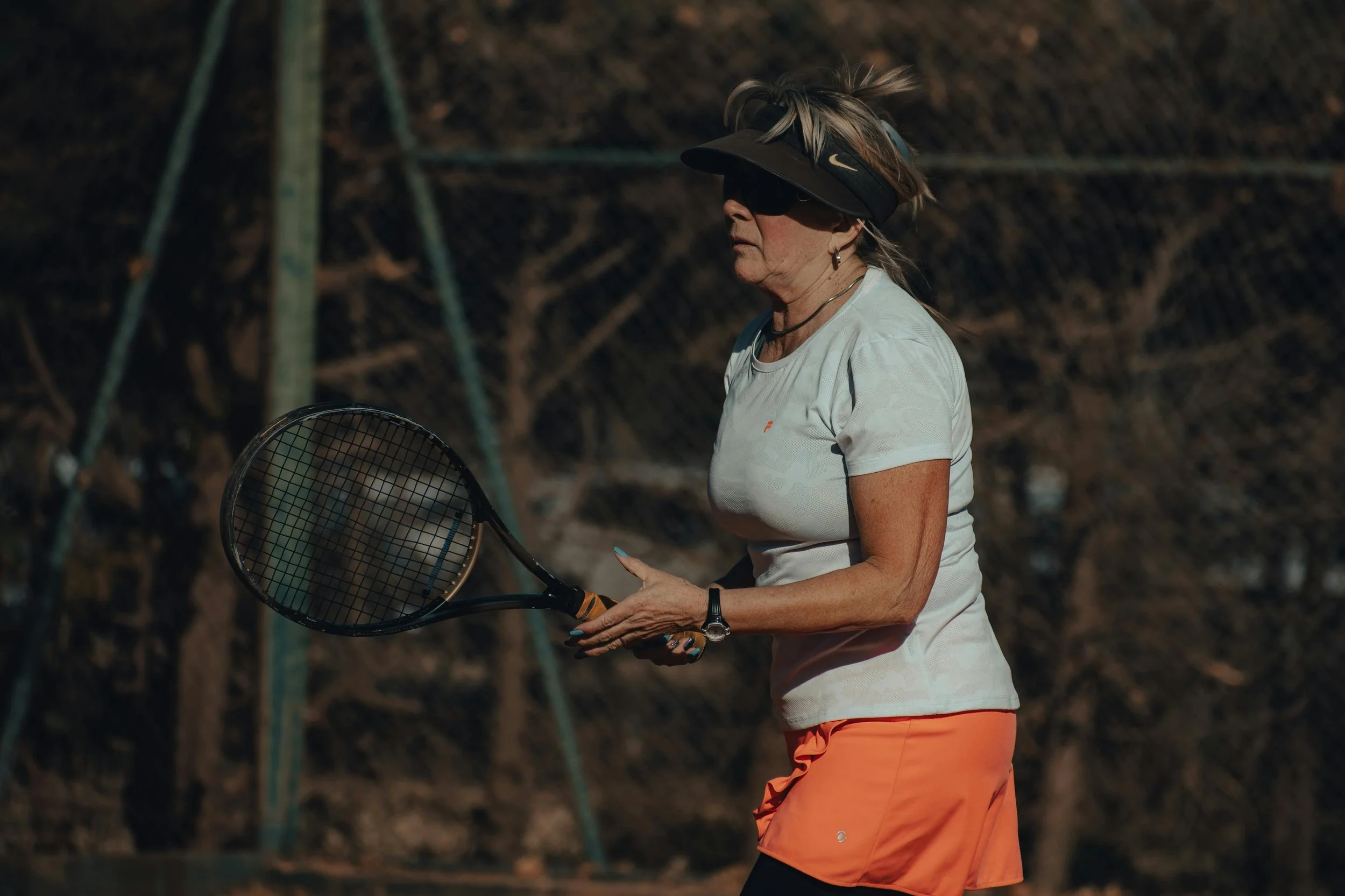 A woman in white t-shirt and orange skirt playing tennis