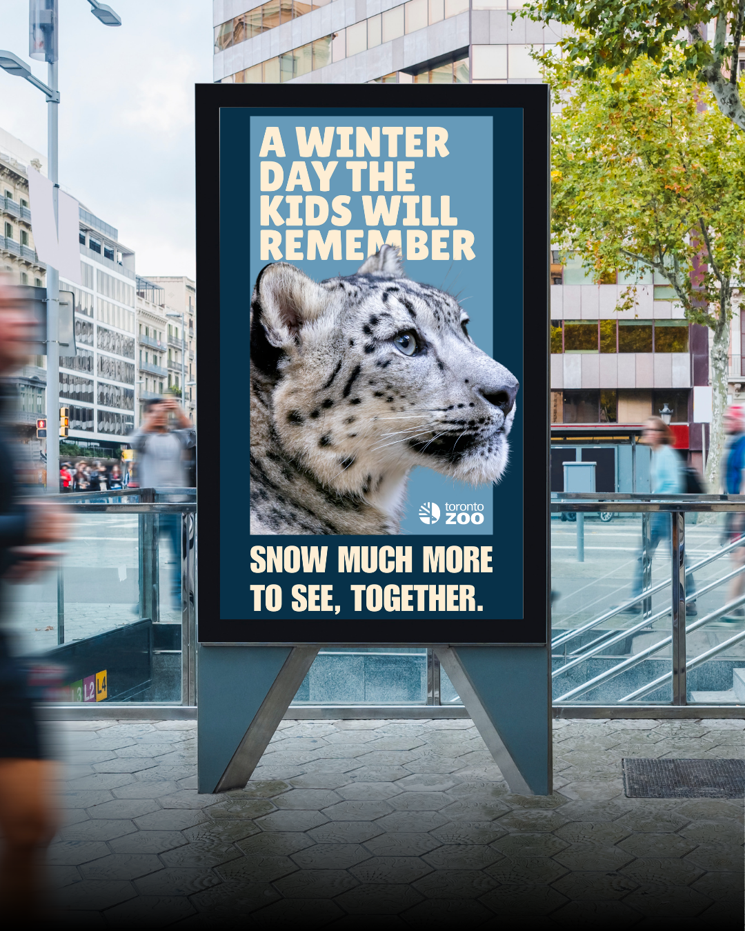 An advertisement for the Toronto Zoo featuring a snow leopard with the message: "A winter day the kids will remember. Snow much more to see, together." The sign has the zoo's logo and is displayed outdoors in an urban setting near buildings and trees.