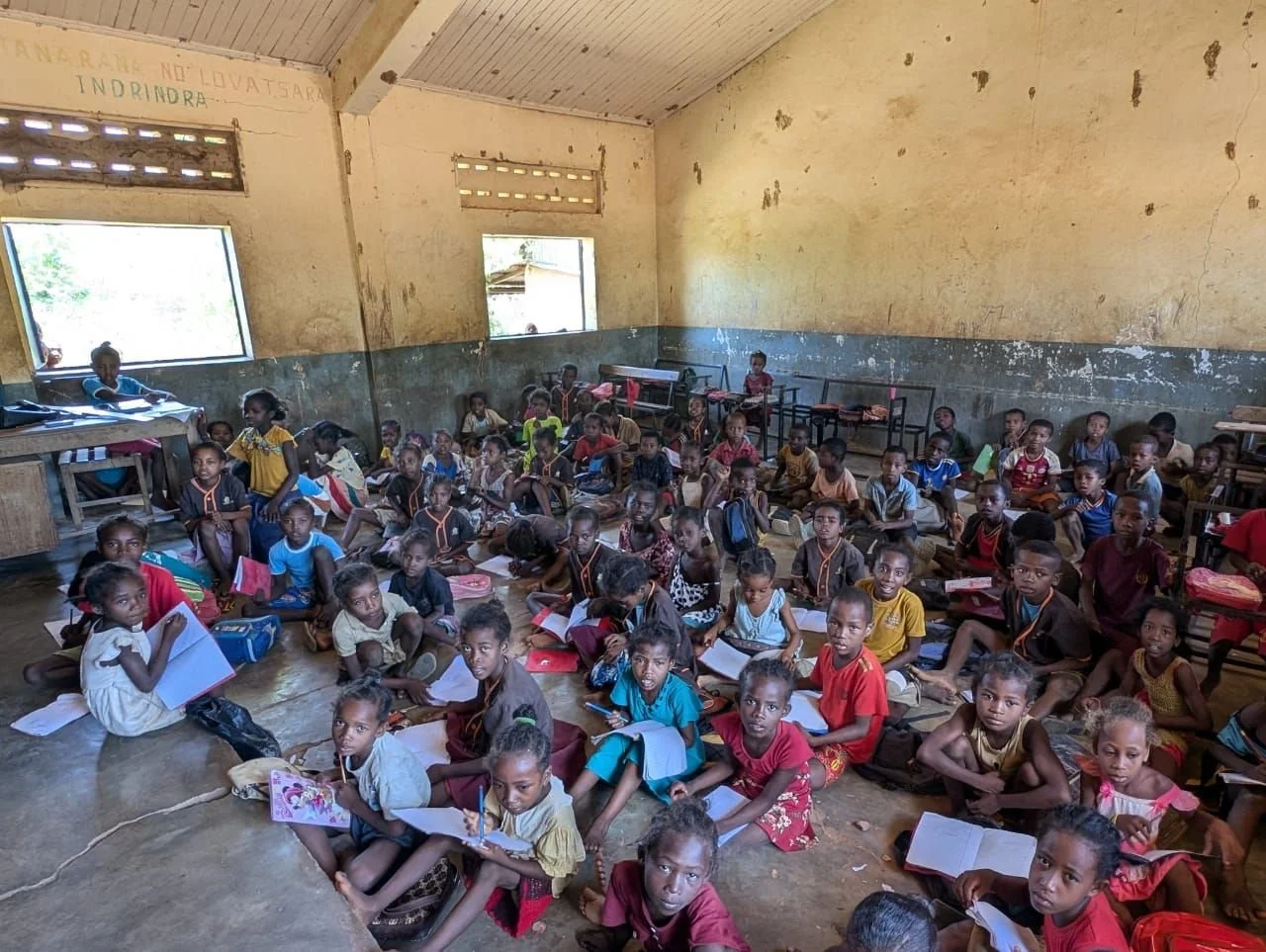 Group of schoolchildren sitting on the floor of a classroom with notebooks and backpacks.