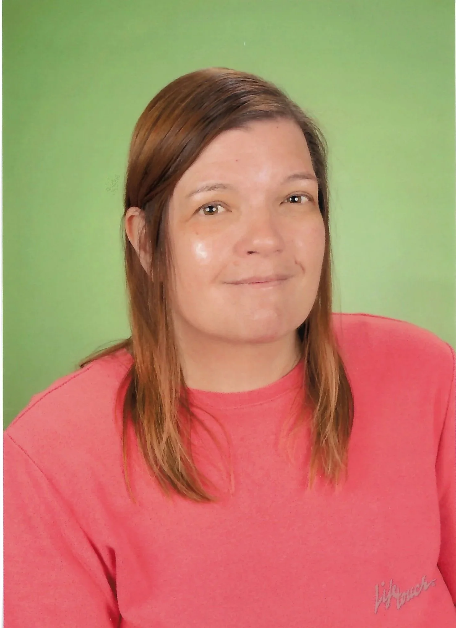 A woman with medium-length brown hair, wearing a pink shirt, smiling subtly, in front of a plain green background.