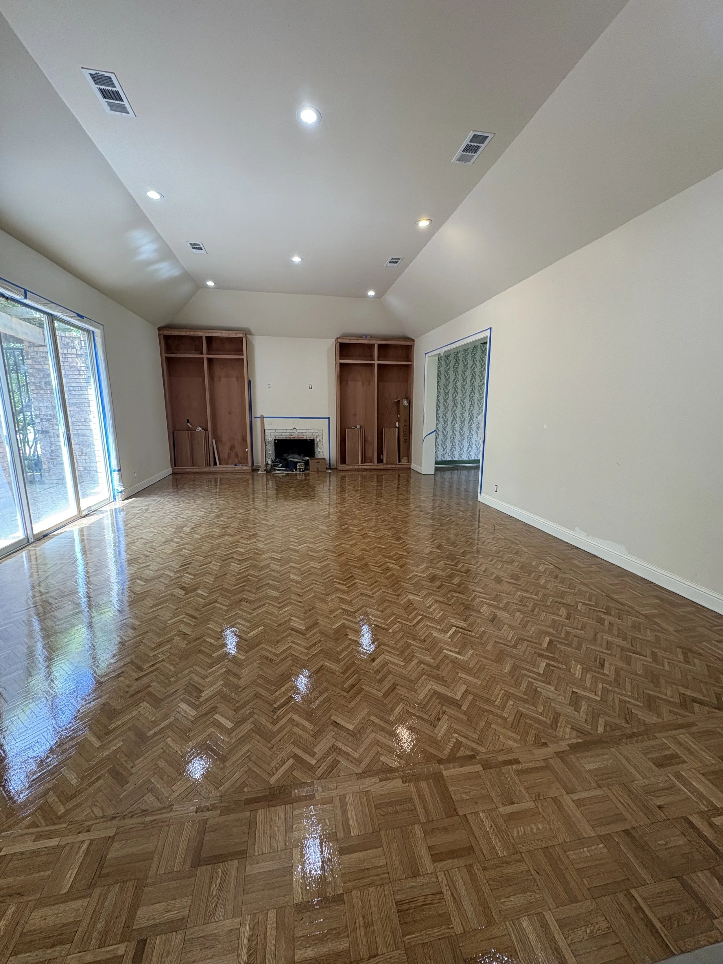 Empty living room with wood flooring, a fireplace, and sliding glass doors. The room is under renovation with blue painter's tape around doorways and windows.