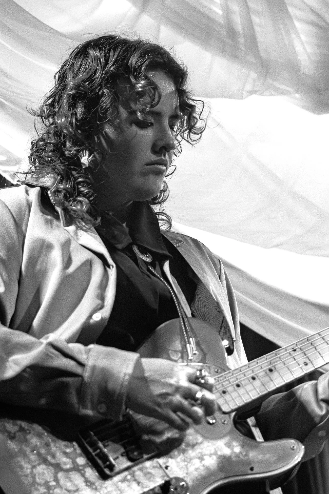 A black and white photo of a woman with curly hair playing an electric guitar.