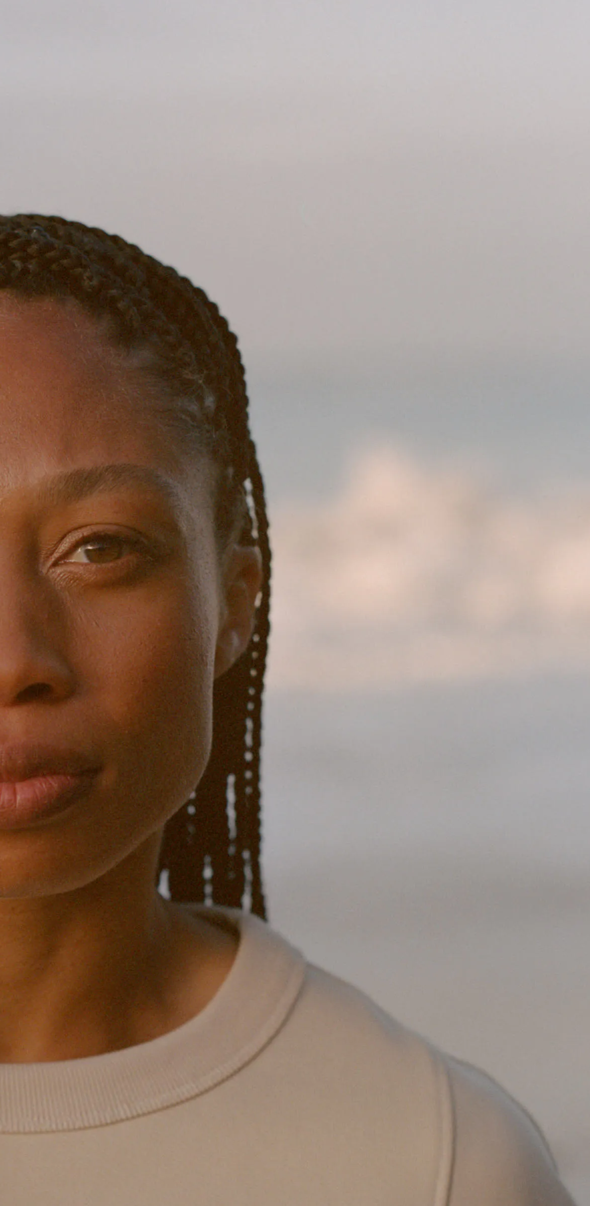Close-up of a young woman with braided hair, wearing a light-colored shirt, with a plain background.