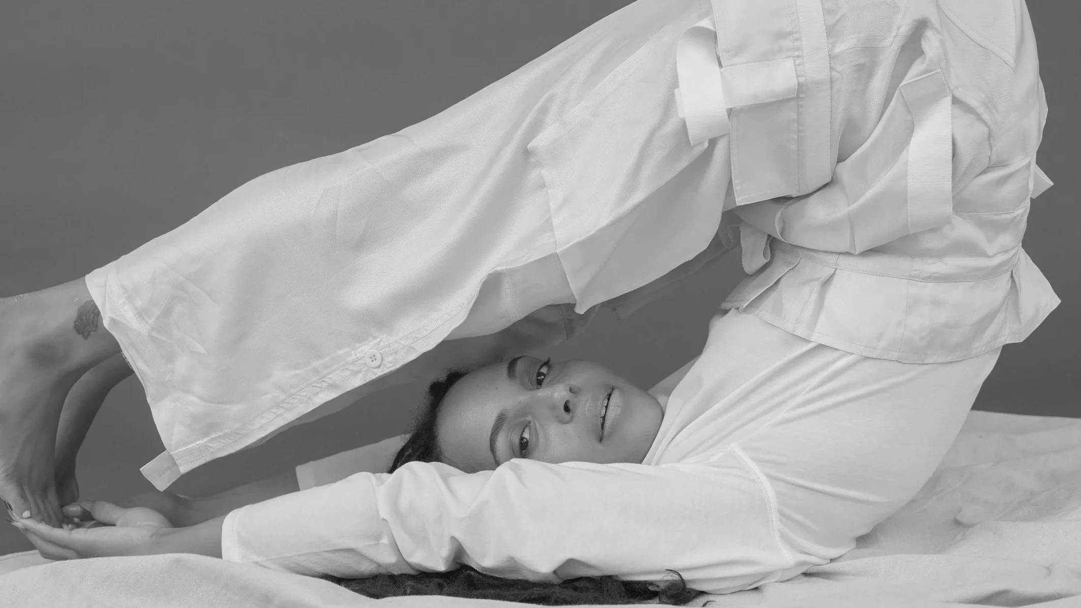 A woman lying on a medical bed, receiving a vaccination from a healthcare professional dressed in white. The woman is smiling, and they are both wearing white medical attire.