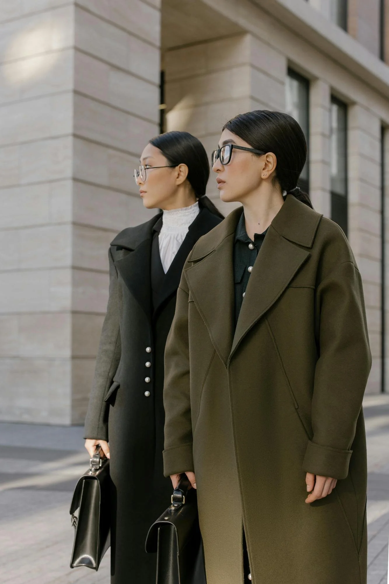 two women in wool coats and glasses looking off to the side