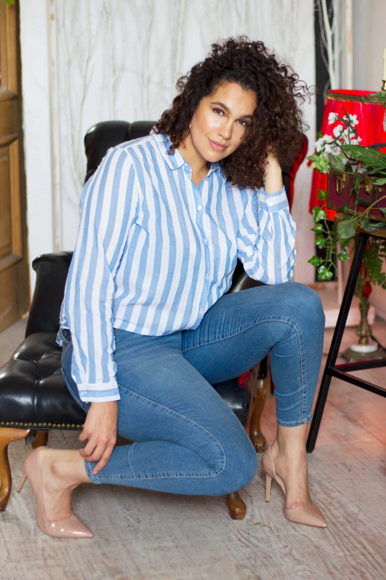 Dariana Casado in blue jeans, blue and white striped shirt and heels, sitting in black chair