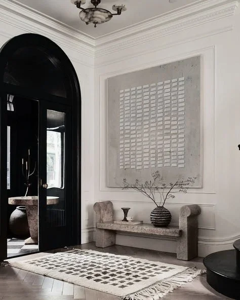entry way room with rug, minimal wall art, bench with vase leading to other room with arched entryway