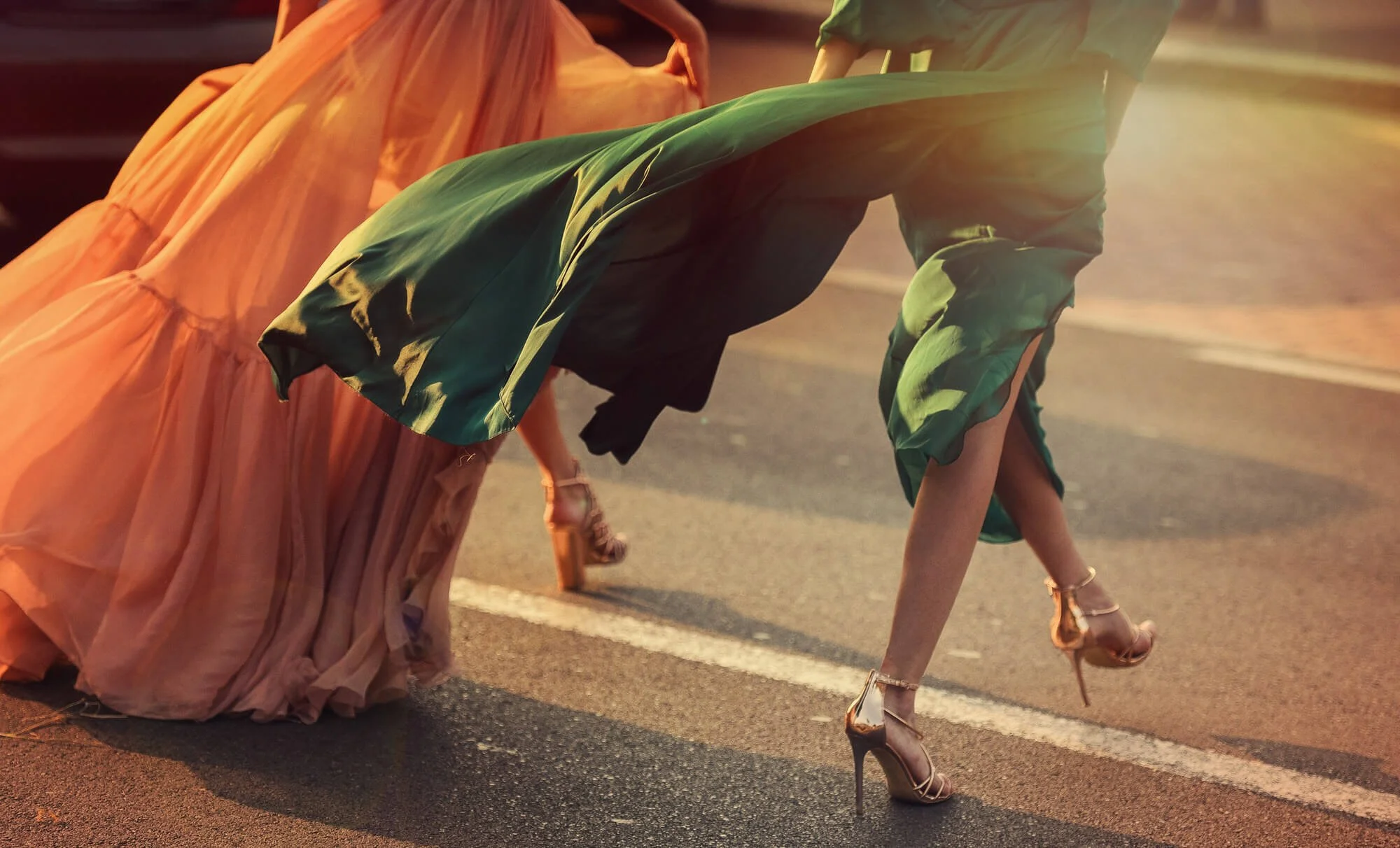 two women walking in heels orange dress and green dress