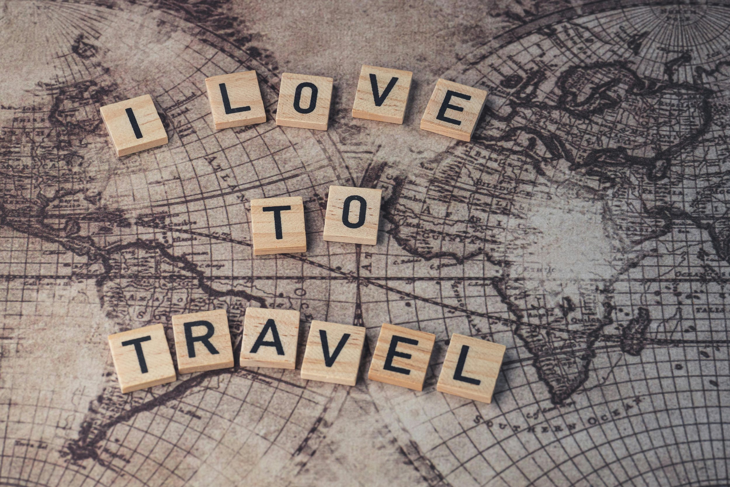 Wooden letter tiles spelling 'I LOVE TO TRAVEL' placed on an antique world map.