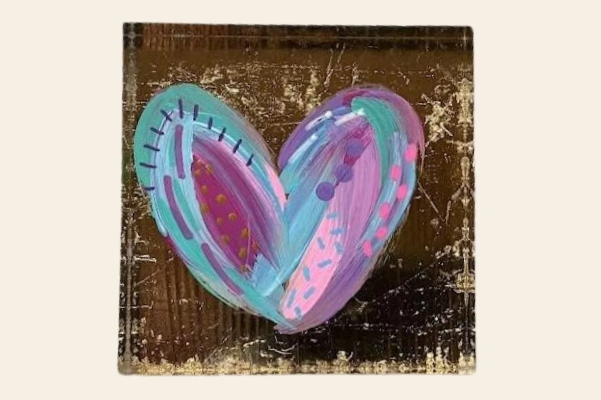 Colorful heart painted on a wooden surface with shades of purple, pink, teal, and yellow.