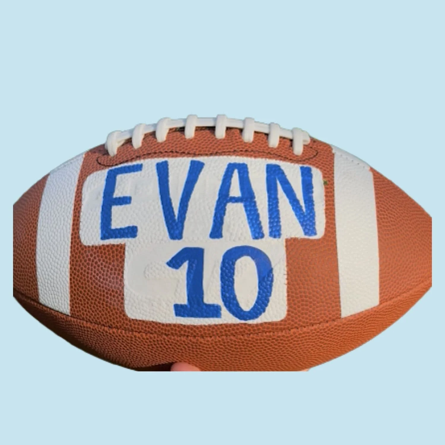 A close-up of a custom American football with the name 'Evan' and the number '10' written on it in blue marker.
