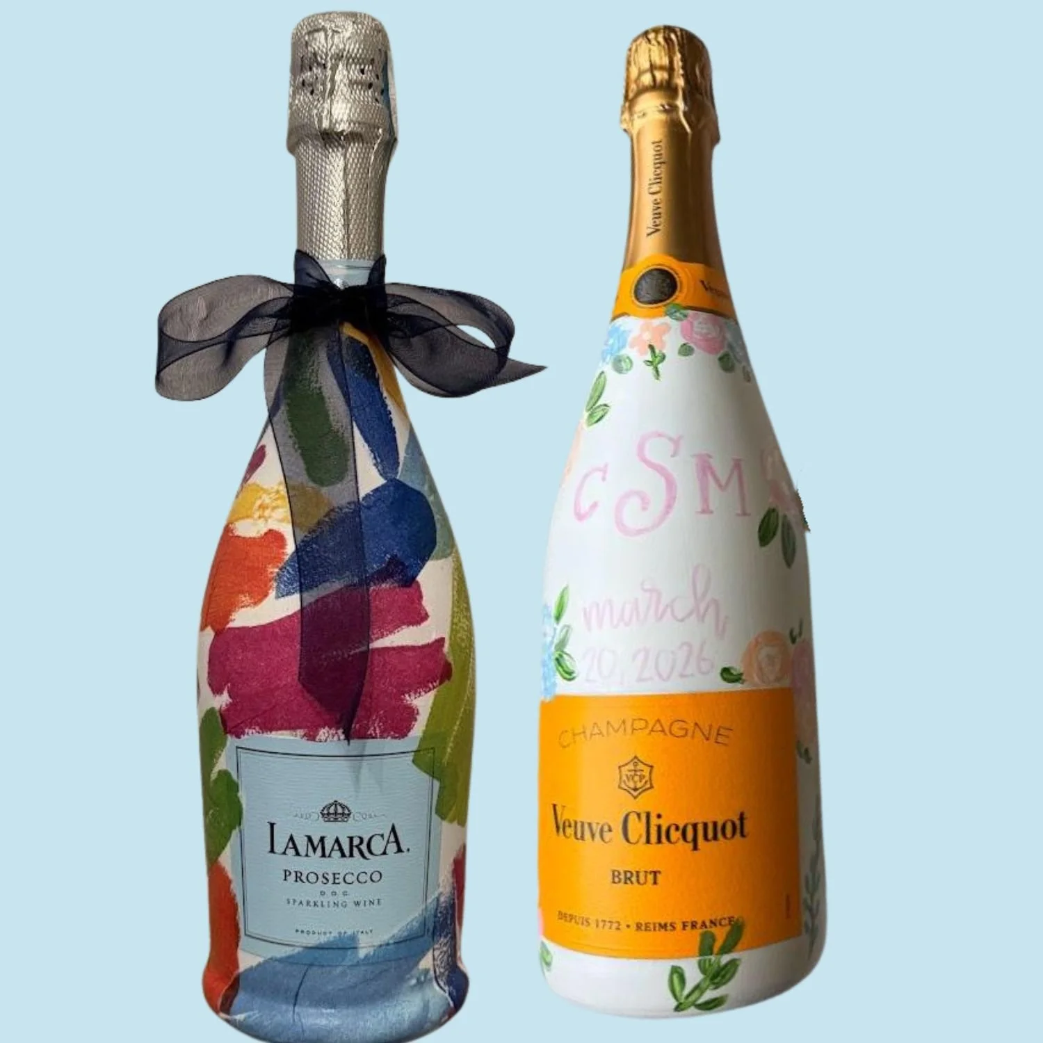 Two customized bottles of sparkling wine, one labeled La Marca Prosecco with a colorful floral label and black ribbon, and the other Veuve Clicquot Brut with a floral and personalized label.