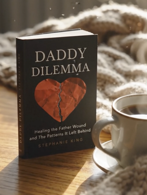 A book titled "Daddy Dilemma" by Stephanie King resting on a wooden surface next to a cup of coffee, with a cozy blanket in the background.
