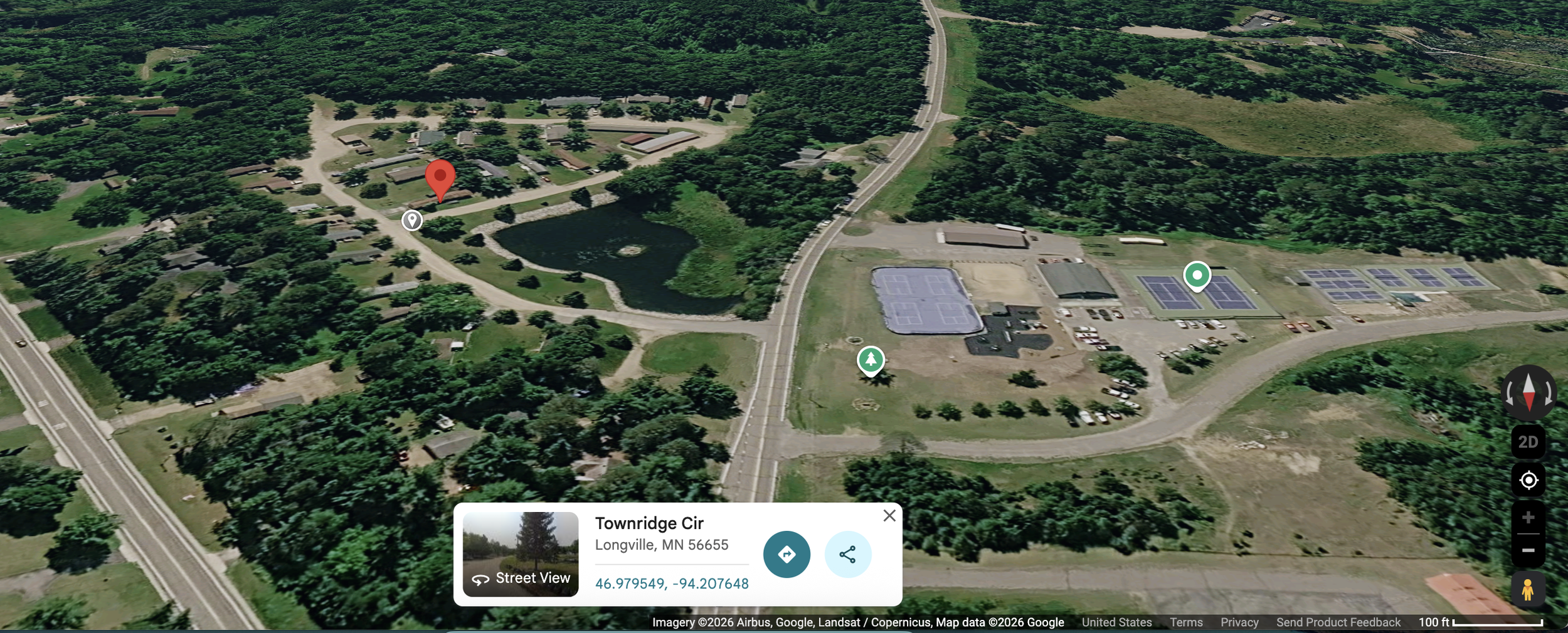 Aerial view of a park with a pond, surrounded by trees, residential buildings, a basketball court, tennis courts, and parking areas in Longville, Minnesota.