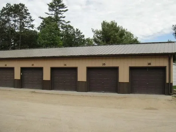 A row of five garage doors numbered 12 to 16, in a beige building with a metal roof, surrounded by trees.