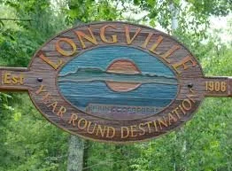 Wooden sign for Longville, marking it as a one-year-round destination established in 1966, with a painted scene of a sunset over water and trees.